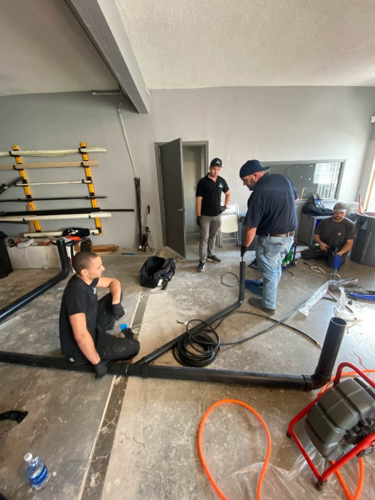 Precision Plumbing crew assembling large-diameter drain-waste-vent pipe on a commercial job site