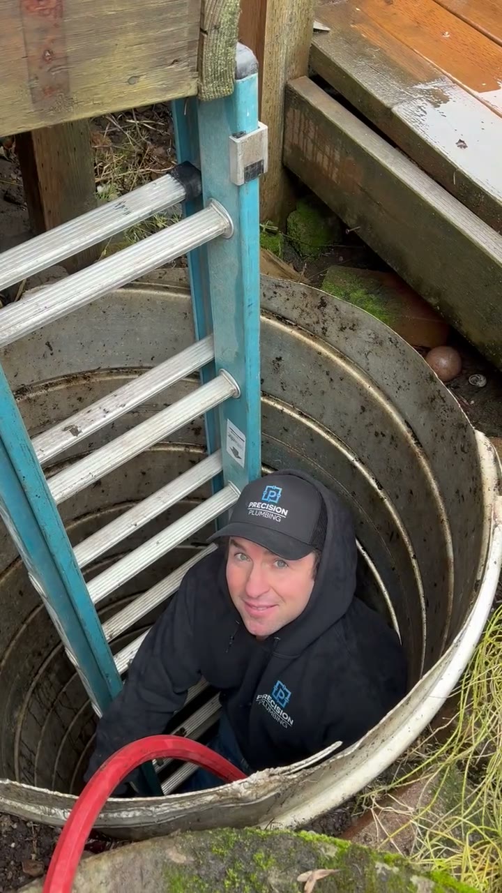 Precision Plumbing technician standing inside a concrete sewer vault with a ladder and hose