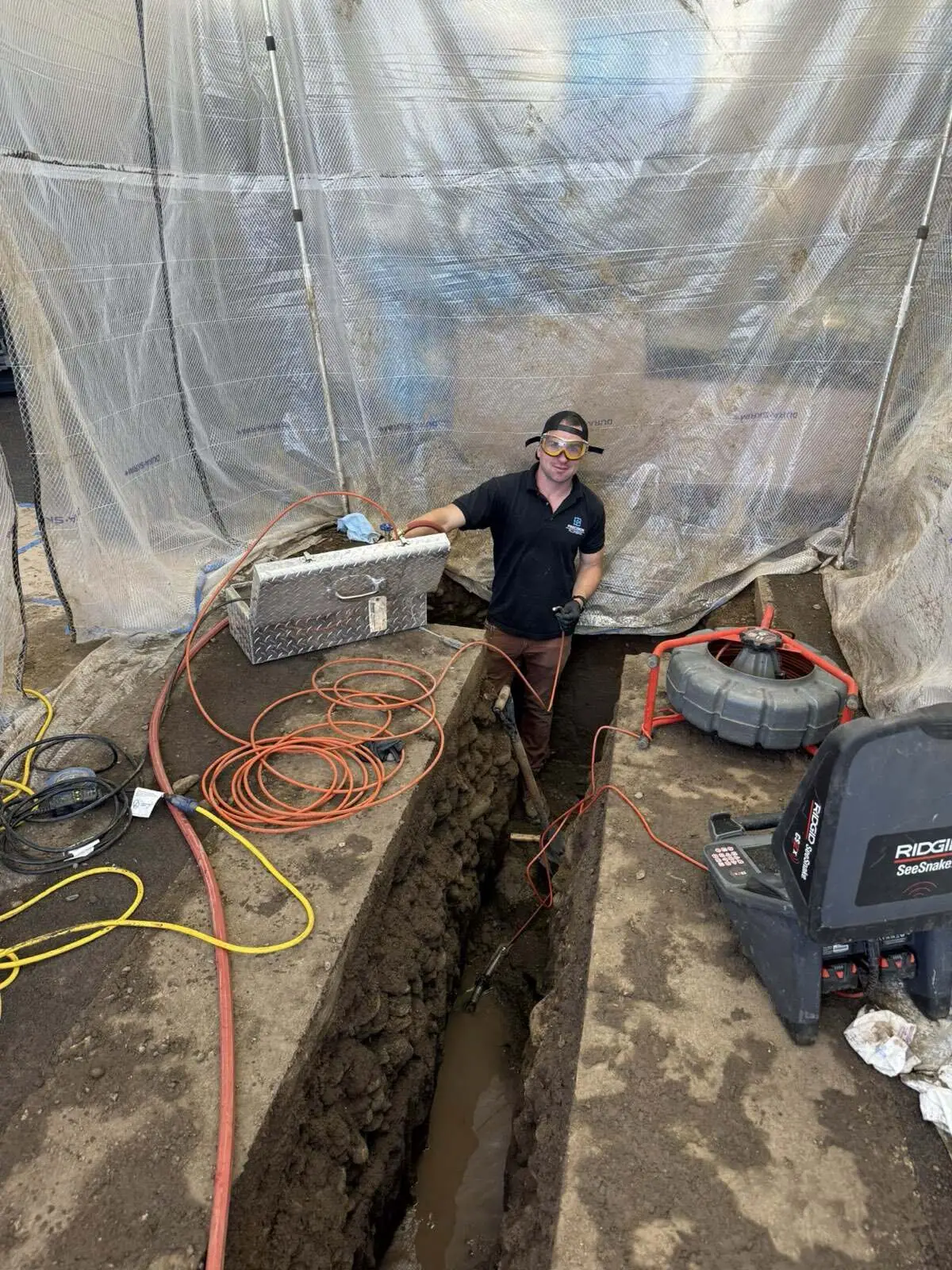 Precision Plumbing technician running a sewer camera inspection at an open trench
