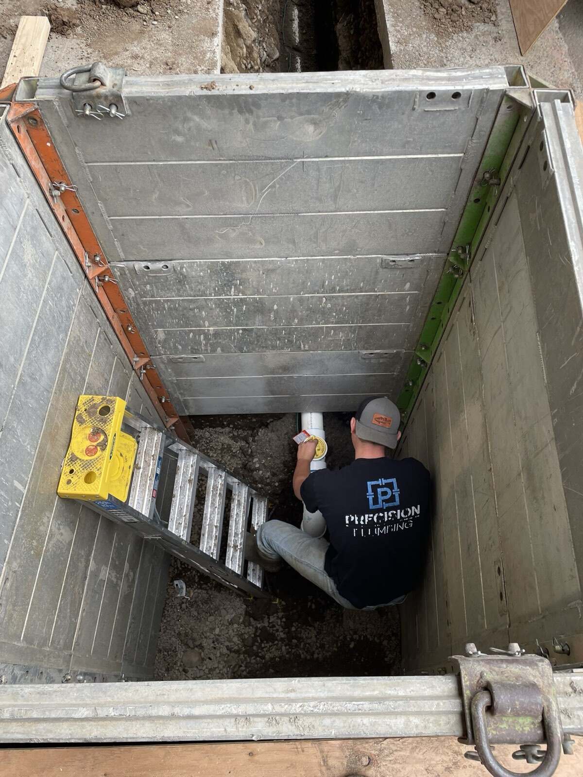 Precision Plumbing technician working in a shored trench box during a sewer line replacement