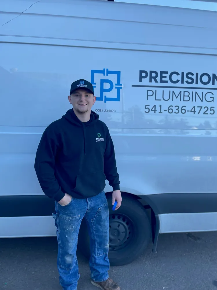 Technician taking a call beside a Precision Plumbing van