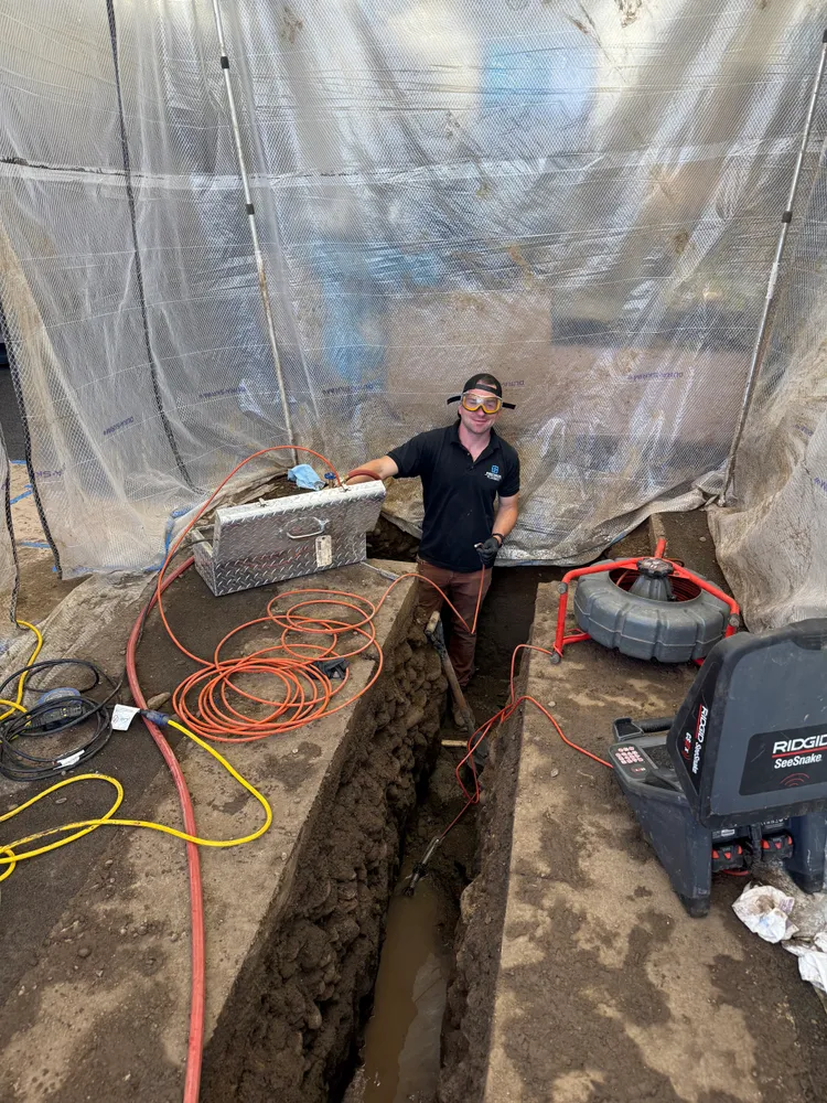 Technician with a sewer camera beside an open trench
