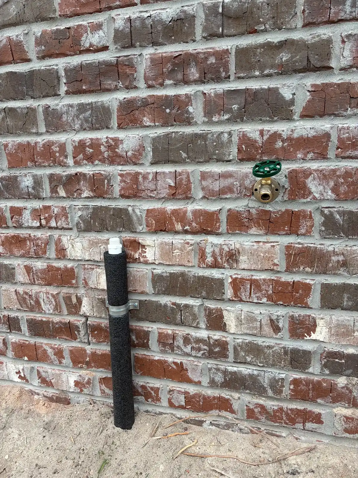 Exterior hose bib and supply piping mounted on a brick home