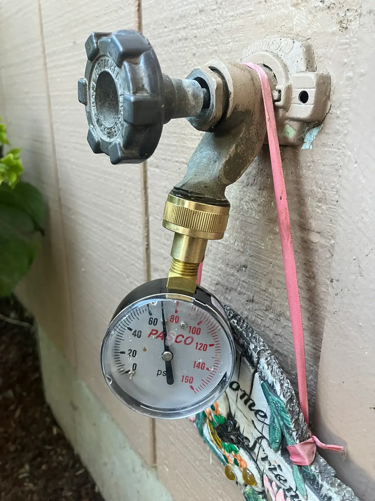 Water pressure gauge attached to an exterior hose bib during a pressure test